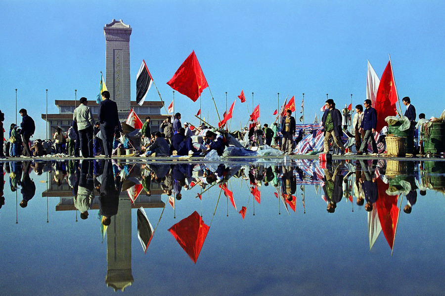 Morning activity in Beijing's Tiananmen Square is reflected in the wet pavement following a downpour. In the background are the Martyrs monument and beyond that Mao's mausoleum. © 1989 AP Photo/Mark Avery