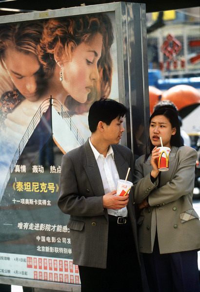 A Chinese couple enjoy a Coke from McDonalds next to a poster for the movie "Titanic" in Beijing. © 1998 Mark Avery/Orange County Register